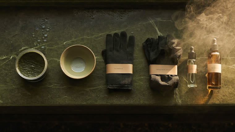 Les cinq produits du rituel alignés dans l'ordre sur un banc de pierre olive humide : savon noir, gant, ghassoul, eau de rose, huile d'argan