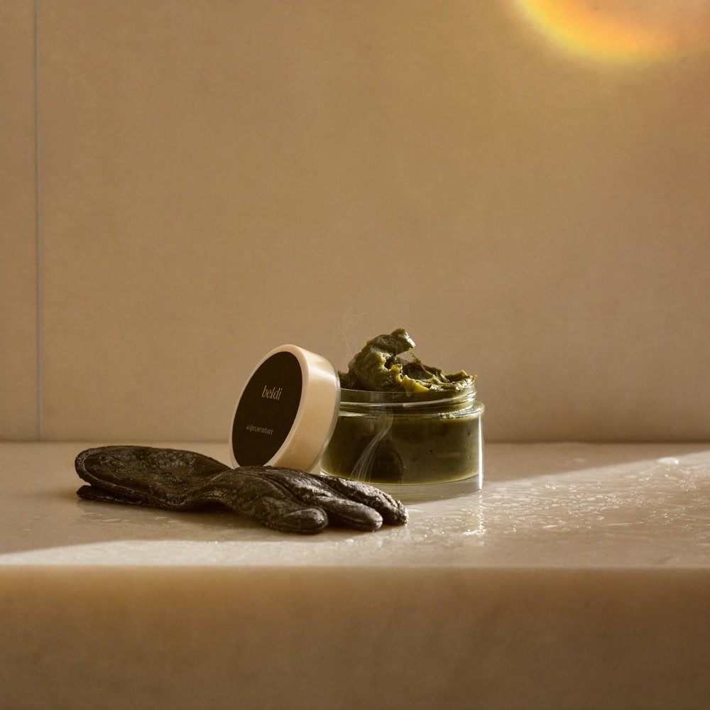 Pot en verre de savon noir beldi vert olive et gant kessa posés sur la pierre humide d'un hammam